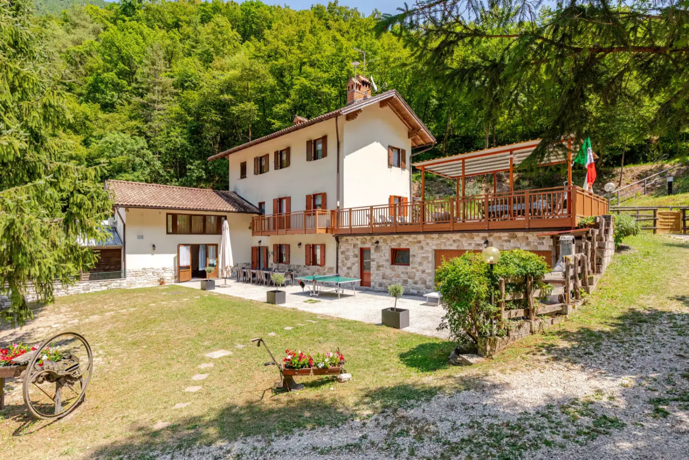 A white Italian villa with wooden shutters and a terrace among green wooded hills in Ala, Trentino